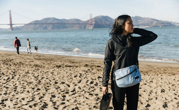 Person wearing the Design Lab Edition Packing Cube Shoulder Bag in Acuity blue while standing on a beach in San Francisco.